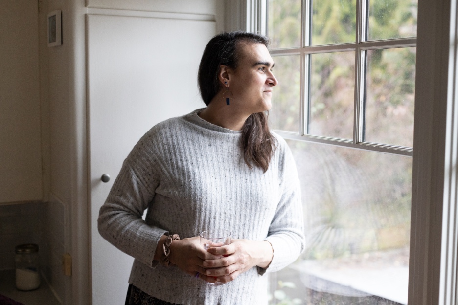 Persona no binaria mirando por la ventana en un momento de reflexión y pausa terapéutica